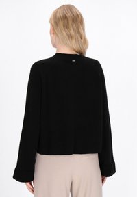 Sort cropped sweater med ribbet tekstur, lange ærmer og rund udskæring. Har en lille metal logo detalje på ryggen.
