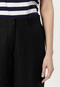 Black linen trousers with a flat waistband and subtle side pockets. Paired with a navy and white striped top. Smooth texture and relaxed fit.