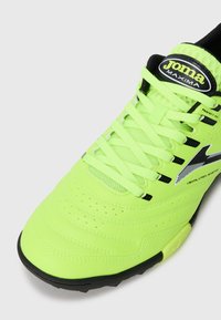 Zapato de fútbol verde neón con parte superior sintética texturizada, logo en negro y blanco, cordones a juego y suela de goma con patrones de tracción.