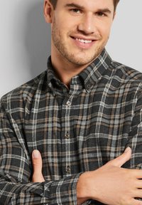 Kariertes Flanellhemd mit Knopfverschluss in Schwarz, Grau und Braun. Weicher Stoff mit Kragen, langen Ärmeln und braunen Knopf-Akzenten.