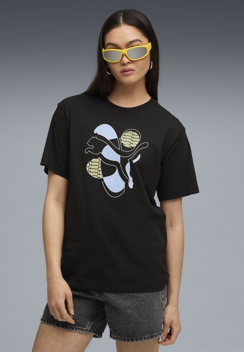 Black cotton t-shirt featuring a stylized Puma logo in light blue and yellow accents. Model wears grey denim shorts and yellow sunglasses.