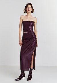 Completo a due pezzi composto da un top corto senza spalline e una gonna aderente con spacco alto, entrambi in ecopelle bordeaux intenso con una texture liscia.