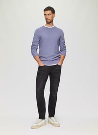 Lichtpaarse textuurtrui met een witte halslijn, gedragen met zwarte slim-fit jeans en witte sneakers met beige accenten.