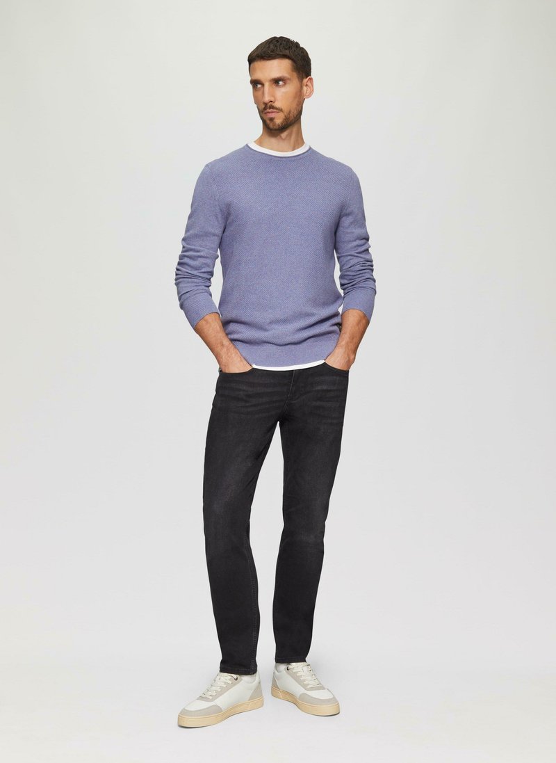Lichtpaarse textuurtrui met een witte halslijn, gedragen met zwarte slim-fit jeans en witte sneakers met beige accenten.