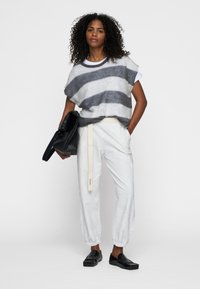 Maglione oversized a righe grigie e bianche in lana, abbinato a pantaloni grigi chiari con polsini elasticizzati. La modella tiene una borsa in pelle nera. Scarpe basse nere.