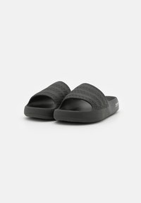 Chinelas pretas com parte superior texturizada com riscas horizontais, sola de borracha macia e design de dedo aberto. Forma plana e minimalista.