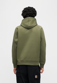 Φούτερ χακί με μεγάλη κουκούλα, ριμπ μανσέτες και τελείωμα. Μαλακό ύφασμα από βαμβακερό μείγμα, μινιμαλιστικός σχεδιασμός, χωρίς ορατά λογότυπα ή διακοσμήσεις.