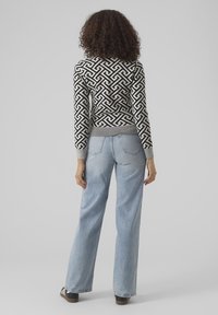 Schwarz-weiß gemusterter Pullover mit geripptem Saum, getragen zu hellblauen Jeans mit geradem Bein und braunen Schuhen, von hinten gesehen.