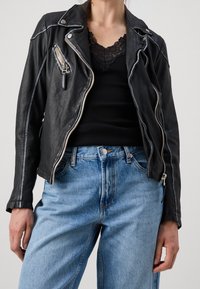 Black leather biker jacket with silver zippers, featuring a fitted design and textured finish, paired with light blue high-waisted jeans.