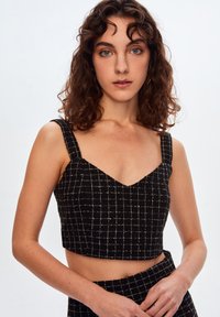 Sort cropped top med V-hals, brede stropper og et rutemønster i hvide tråde. Den strukturerede stof giver dybde til designet.