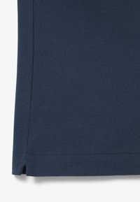 Tissu texturé bleu foncé avec une couture cousue et une petite fente latérale près du bord inférieur.