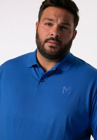 Modrá polo tričko s límečkem, třemi knoflíky a decentním embosovaným logem na hrudi. Hladká textilie. Standardní střih.