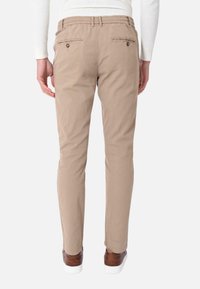 Chino beige con vestibilità slim, caratterizzati da una vita piatta, due tasche posteriori con chiusura a bottone e una cintura intrecciata. Tessuto in cotone morbido, texture liscia.