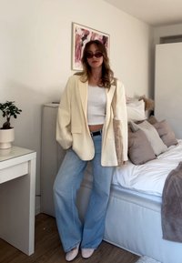 Kremowa, obszerna marynarka na białym topie crop, połączona z jasnoniebieskimi szerokimi spodniami dżinsowymi i cielistymi szpilkami. W zestawie znajduje się pleciona torba i wnętrze.