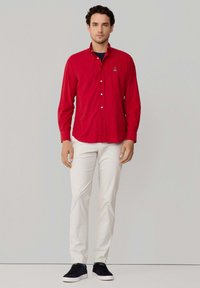 Rode langemouwen knoopshirt met een kraag, gecombineerd met witte broek en zwarte sneakers. Features een geborduurd logo op de borst.