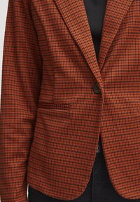 Oranje en zwart geblokte blazer met een geknopt revers, twee voorzakken, een enkele knoopsluiting en een gestructureerde stof.