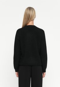 Pull en laine noir tricoté avec des manches côtelées, un col rond et une coupe décontractée. Texture douce avec un ourlet standard et une couleur unie.