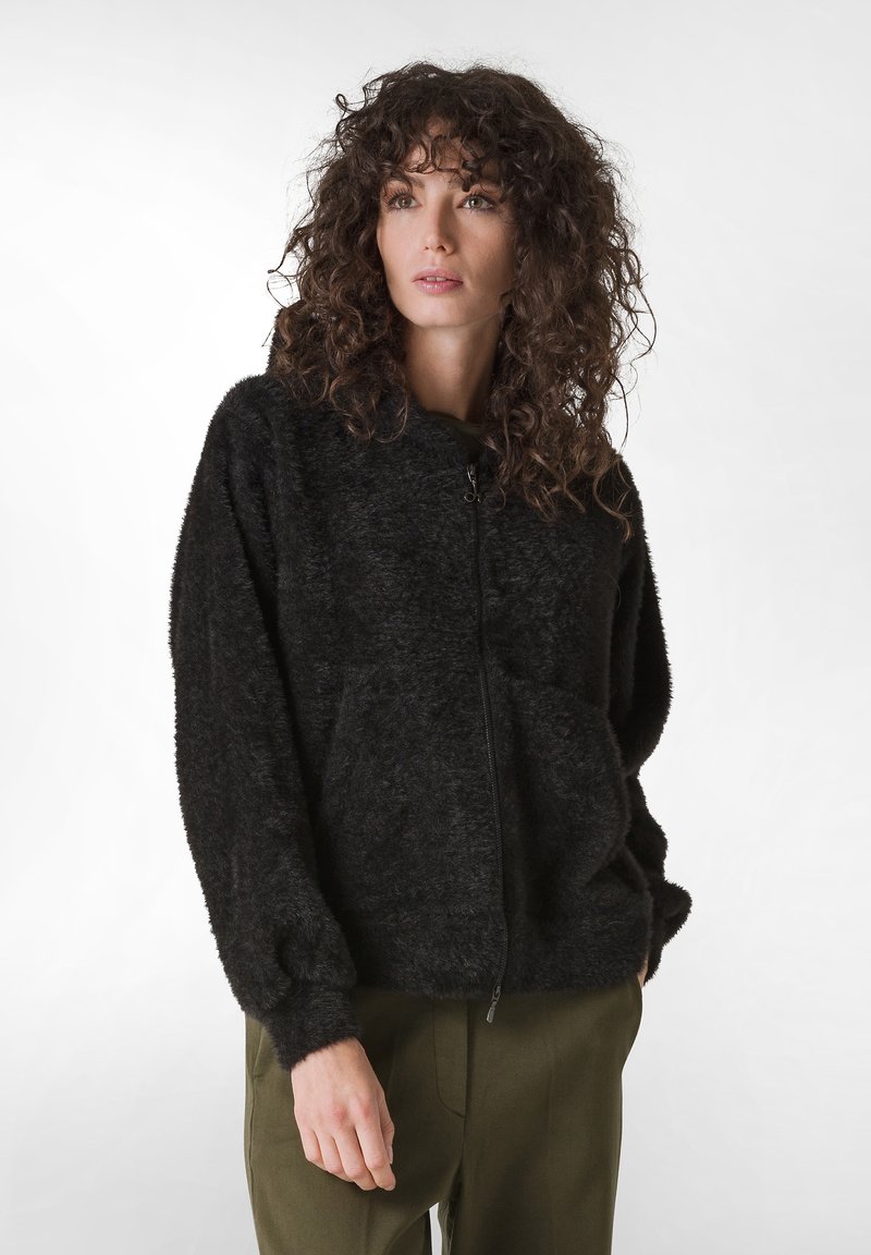 Giacca nera soffice con zip e cappuccio, caratterizzata da polsini a costine e una vestibilità rilassata. La superficie liscia e le tasche laterali ne migliorano la funzionalità.