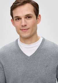 Szary sweter w serek wykonany z miękkiej dzianiny. Posiada małe logo s.Oliver, noszony na białym t-shircie z okrągłym dekoltem.