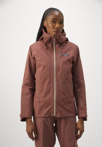 Patagonia damesjakke i mørk rosa farve, med høj krave, flere lynlåse og et slankt, vandtæt design.