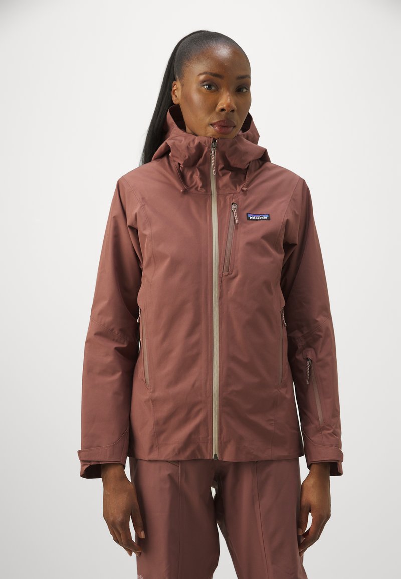 Patagonia damesjakke i mørk rosa farve, med høj krave, flere lynlåse og et slankt, vandtæt design.