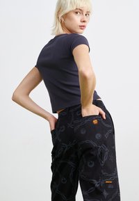 Pantaloni cargo neri con un motivo sottile, dotati di grandi tasche e un logo rosso. La t-shirt aderente blu navy ha maniche corte e un collo rotondo.