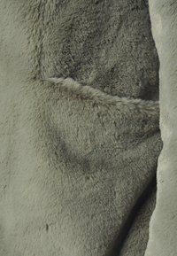 Närbild av mjuk, grå pälsstruktur med en synlig söm eller vik som skapar djup och kontrast i tyget.