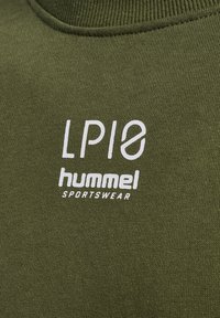 Gros plan d’un tissu tricoté vert olive avec les logos blancs « LP10 » et « hummel SPORTSWEAR » imprimés sur la zone de la poitrine.
