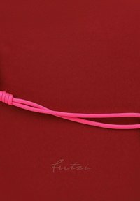 Una tela roja con una textura suave presenta un prominente detalle de cordón rosa. El nombre de la marca "fuitzi" está sutilmente impreso en el fondo.