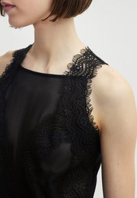 Zwarte mouwloze top met een ingewikkelde zwarte kantafwerking langs de schouders, gemaakt van een transparante, gladde stof. Elegant ontwerp met delicate texturen.