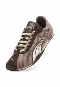 Καφέ αθλητικό παπούτσι Puma από δίχτυ με λευκές πλευρικές ρίγες, μπεζ κορδόνια και υφή στη σόλα, τοποθετημένο σε γωνία πάνω σε λευκό φόντο.