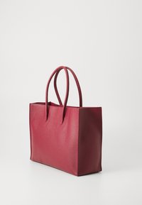Rød læder tote taske med en tekstureret overflade, der har to forlængede håndtag og en rektangulær form. Minimalistisk design, ingen synlig hardware.