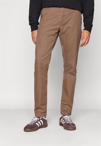 Bruna bomullschinos med en något texturerad yta, rak skärning och sidofickor, kombinerat med lila sneakers med vita ränder.