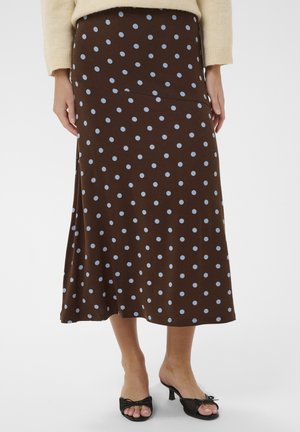 Brązowa spódnica midi w jasnoniebieskie groszki, noszona z beżowym swetrem i czarnymi sandałami na obcasie z odkrytymi palcami na jednolitym tle.