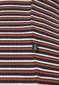 Ribbad topp med horisontella ränder i röd, vit och marinblå. Inkluderar en liten svart etikett vid sömmen. Mjuk, texturerad tyg.