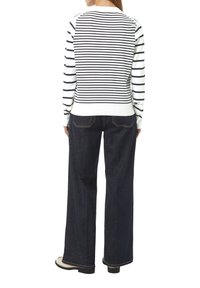 Gestreifter Pullover in Weiß und Marineblau, mit langen Ärmeln und einem gerippten Saum, kombiniert mit weit geschnittenen dunklen Jeans und schwarzen Schuhen.