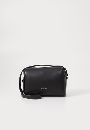Petit sac bandoulière rectangulaire en cuir noir avec logo Calvin Klein argenté et bandoulière réglable sur fond blanc.