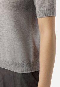 Grå kortärmad tröja i mjukt, lätt material med ribbad halsringning och fåll, kombinerad med mörkgrå byxor.