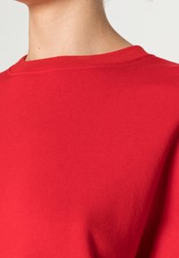 Czerwony bawełniany sweatshirt z okrągłym dekoltem i miękką fakturą. Tkanina wydaje się gładka, o prostym wzornictwie bez widocznych ozdób.