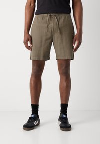 Khaki shorts med snøre i taljen, kort længde og struktureret stof. Stylet med sorte træningssko og sorte sokker.