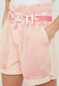 Pantalones cortos de color rosa claro hechos de tela texturizada, con cintura con cinturón, bolsillos laterales y patrones sutiles de teñido anudado.