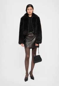 Faux fur black cropped jacket, black long-sleeve top, brown leather skirt, sheer tights, black pointed-toe heels, and a textured black handbag.