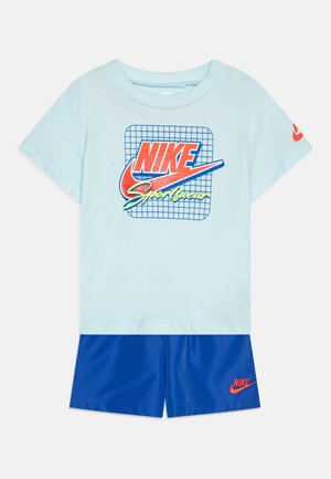 T-shirt in cotone azzurro chiaro con logo Nike retrò e motivo a griglia, abbinato a pantaloni corti blu navy con un piccolo logo Nike arancione.