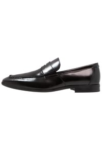 Mocassin pour homme en cuir noir avec petit talon, couture mocassin sur le devant, et une bride sur le dessus, présenté sur un fond blanc.
