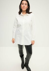 Hvid langærmet skjorte med knaplukning og spids krave samt broderede detaljer på manchetterne, parret med sorte blanke leggings og cowboystøvler.