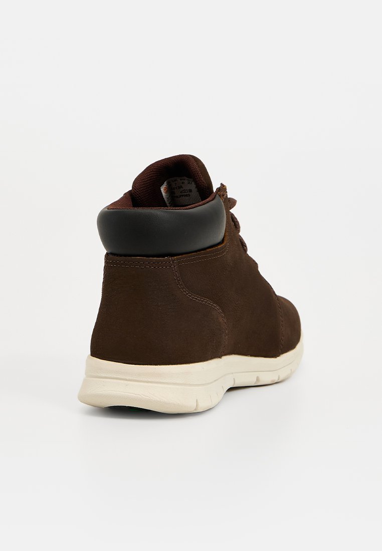 Zapatillas altas de ante marrón con un cuello acolchado negro, suela de goma blanca y panel trasero texturizado. Cordones y logo visibles en la lengüeta.