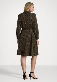 Rochie neagră cu un model circular în tonuri de aur și crem, mâneci lungi, talie accentuată cu curea și fustă evazată. Purtați-o cu pantofi cu toc negri.