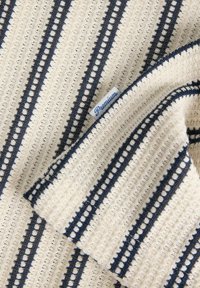 Tissu en tricot crème avec des rayures marine et des détails ajourés. Une petite étiquette "Premium" est attachée au bord.