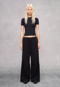 Camiseta negra corta y pantalones de chándal negros de corte holgado, con una cinturilla elástica. Tejido suave con una textura lisa.