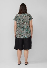 Korte mouwen top in een multicolor geometrisch patroon met zwart, turquoise en crèmekleuren; gecombineerd met losse zwarte shorts en sandaal.